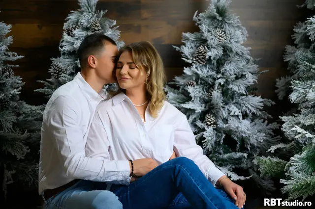Cuplu îmbrățișat în decor de iarnă cu brazi înzăpeziți